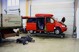 Stor bil i rött med öppen motorhuv i lagerlokal